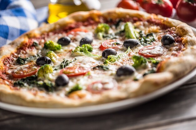 Pizza italiana con broccoli spinaci pomodori olive e mozzarella o parmigiano. Pasto vegetariano mediterraneo.