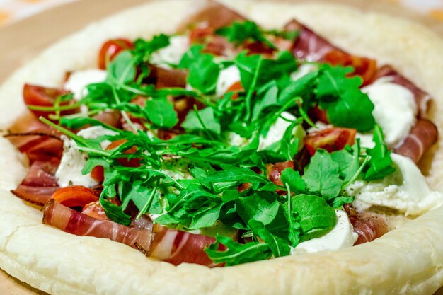 Pizza italiana con mozzarella, pomodoro, pancetta e rucola fresca sul tavolo di legno.