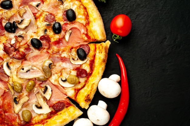 pizza italiana con pancetta, funghi, olive, pomodori su uno sfondo nero di cemento con copia spazio per il testo