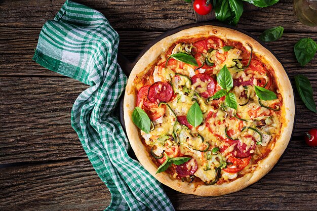 Pizza italiana con pollo, salame, zucchine, pomodori ed erbe
