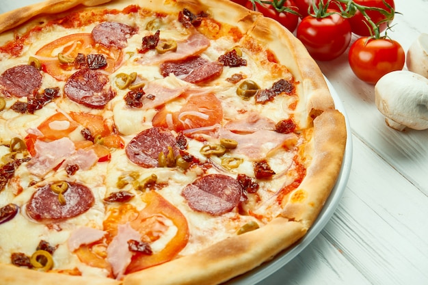 Pizza italiana con salame, prosciutto e olive in una composizione con ingredienti
