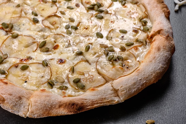 Pizza italiana deliziosa fresca con pera e semi di zucca su uno sfondo di cemento scuro. cucina italiana