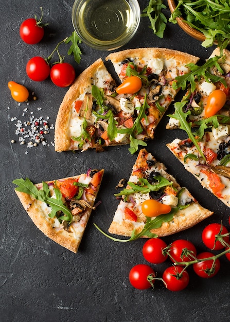 Pizza italiana di verdure con pomodori su sfondo nero, copia spazio, vista dall'alto, verticale