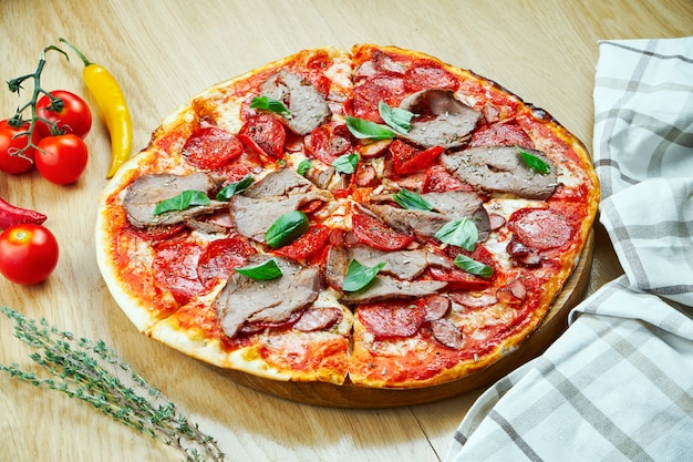 Pizza italiana, fatta in casa con carne, salame e peperoncino su un tavolo di legno.