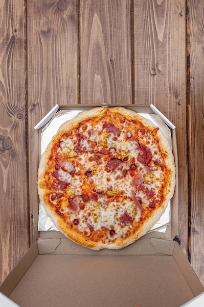 Pizza italiana in una scatola di cartone sulla tavola di legno. Vista dall'alto.