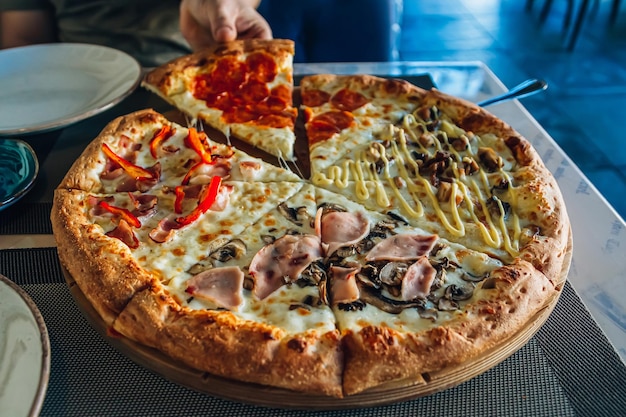 Pizza italiana quattro stagioni su una tavola di legno su un tavolo in un caffè o in un ristorante La mano dell'uomo prende un pezzo di pizza