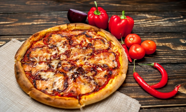 Pizza italiana su un tavolo di legno con ingredienti, pomodori, peperoni, cipolle