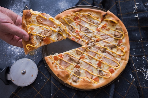 Pizza italiana tradizionale con chiken sul tavolo di pietra blu scuro. L&#39;uomo taglia la pizza con un coltello