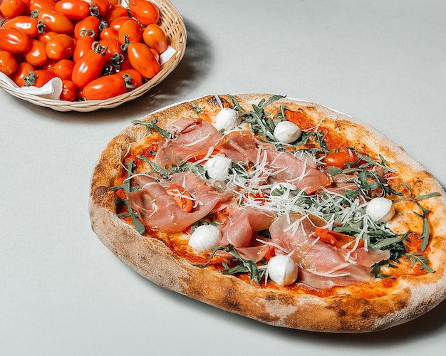 Pizza italiana tradizionale con mozzarella di prosciutto e un piatto di pomodori su sfondo bianco