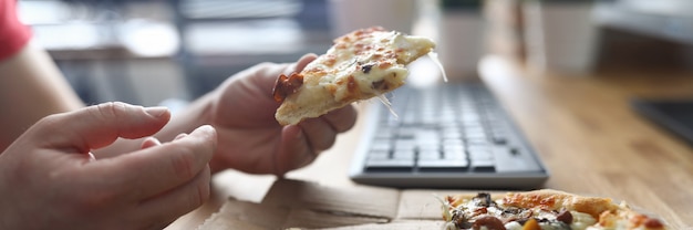 Pizza mangiatrice di uomini in posto di lavoro in computer anteriore