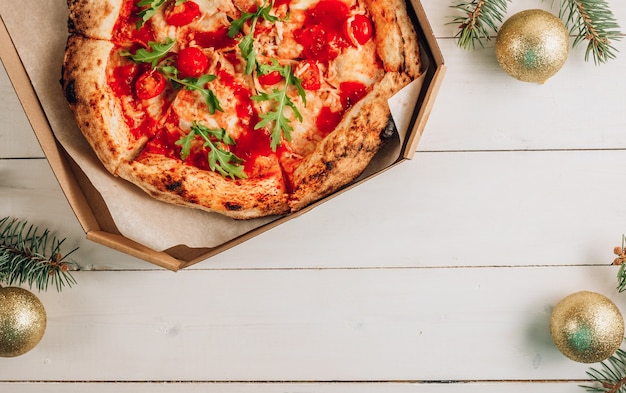 Pizza Margherita con rucola fresca e decorazioni natalizie su legno bianco