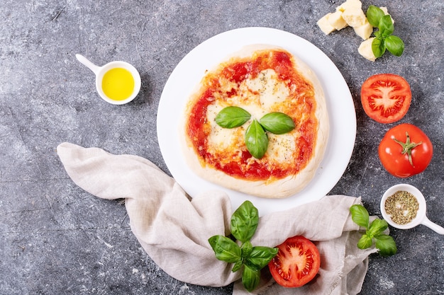 Pizza margherita fatta in casa con mozzerala servita con basilico fresco, spezie, origano e pomodori su una superficie blu. Vista dall'alto, piatto.