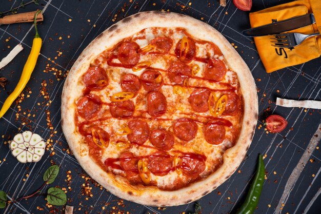 Pizza piccante con salsicce e peperoncini su uno sfondo di pietra nera Spazio libero per il testo