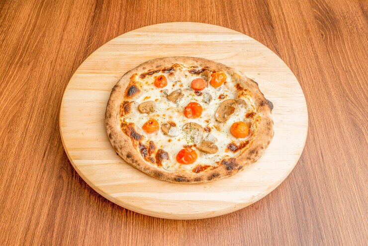 Foto pizza piccola con fette di funghi pomodorini arrostiti interi e tanto formaggio fuso con origano su piatto di legno