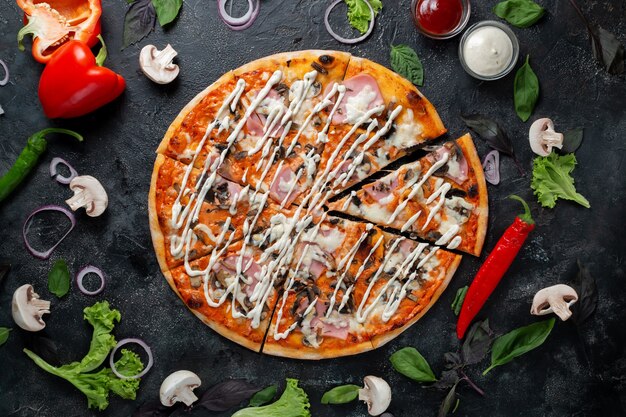 Pizza prosciutto e funghi su fondo scuro con verdure, peperoni, mozzarella e basilico. Vista dall'alto sul tavolo in pietra scura