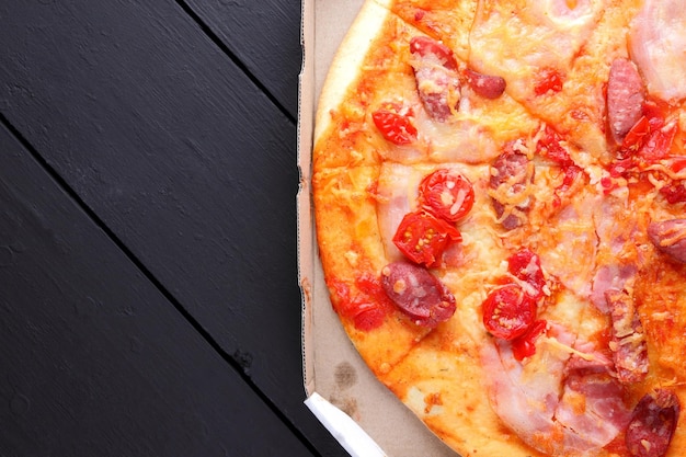 Pizza su fondo di legno nero Pizza italiana con pomodori, salsicce e formaggio su sfondo scuro Cucina italiana Copia spazio