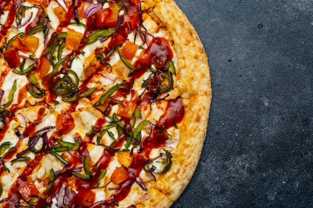 Pizza su uno sfondo scuro. Classica pizza italiana con pomodoro, pepe, verdure, salsa e formaggio mazarella su un tavolo da cucina scuro. Copia spazio