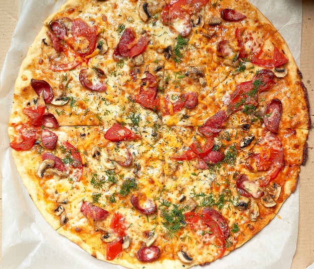 Pizza tonda al forno con salsicce affumicate, funghi, pomodori, formaggio e aneto in una scatola di cartone aperta