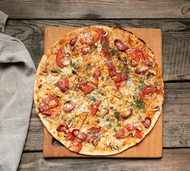 Pizza tonda al forno con salsicce affumicate, funghi, pomodori, formaggio