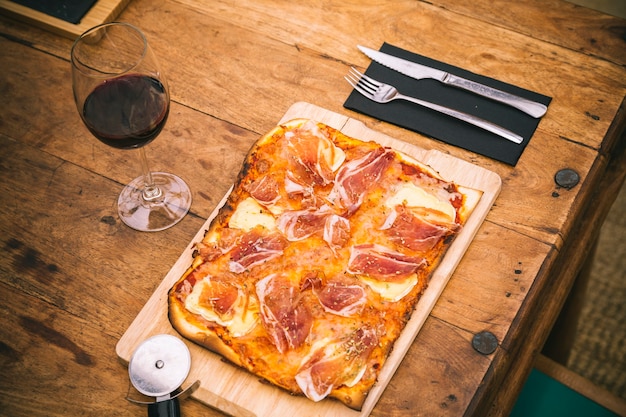 Pizza tradizionale con prosciutto e formaggio brie con bicchiere di vino rosso su tavola rustica