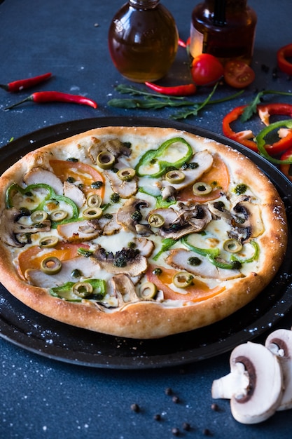 Pizza tradizionale italiana con funghi, pepe e pomodori sul tavolo di pietra blu scuro