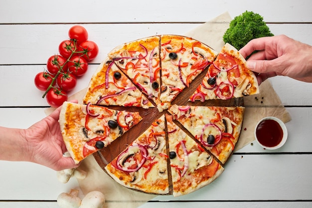 Pizza vegetariana appena sfornata con pomodori, funghi, peperoncino, olive, cipolla e mozzarella servita su fondo in legno con salse ed erbe aromatiche Concetto di consegna del cibo Menu del ristorante