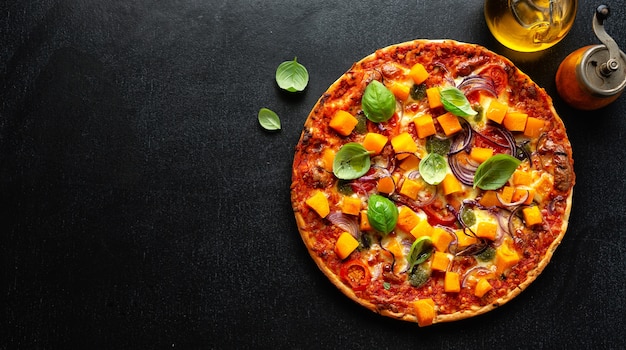 Pizza vegetariana autunnale con zucca e verdure su sfondo scuro. Banner