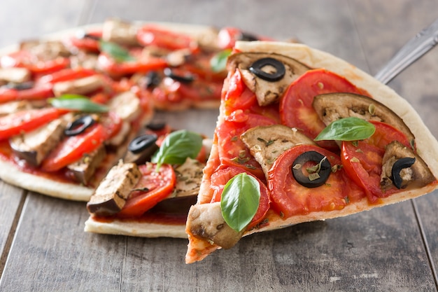 Pizza vegetariana con melanzane, pomodoro, olive nere, origano e basilico su superficie di legno