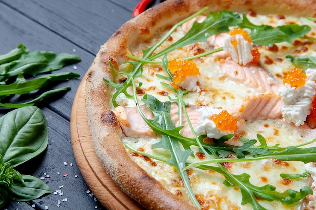 Pizza vista dall'alto con salmone, rucola, caviale rosso, formaggio su fondo di legno scuro con copia sapce. Pizza italiana con frutti di mare. Sfondo di cibo. Gustosa pizza fatta in casa con cucina italiana