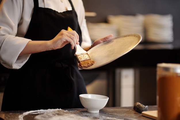 Pizzaiolo che utilizza un pennello sintetico per coprire il vassoio con un sottile strato di olio vegetale