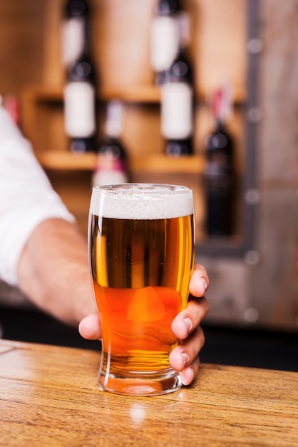 Placa la tua sete! Primo piano dell'uomo che allunga il bicchiere con la birra mentre si trova al bancone del bar