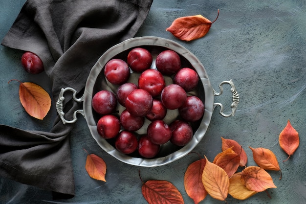 Placca di metallo vintage con prugne rosse e foglie di autunno rosse e arancioni sparse