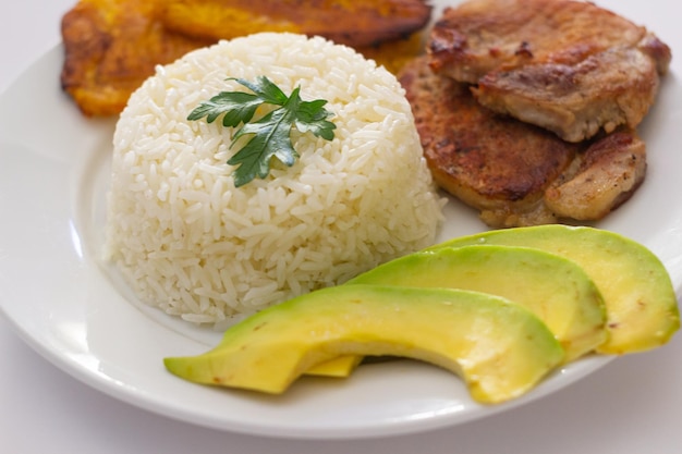 Plato almuerzo dominicano, tostones fritos, arroz blanco acompañados de varios aguacates cortados, comida en casa, toma cerrada.