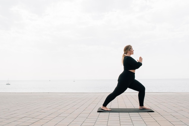 Plus size ragazza che pratica yoga davanti all'oceano