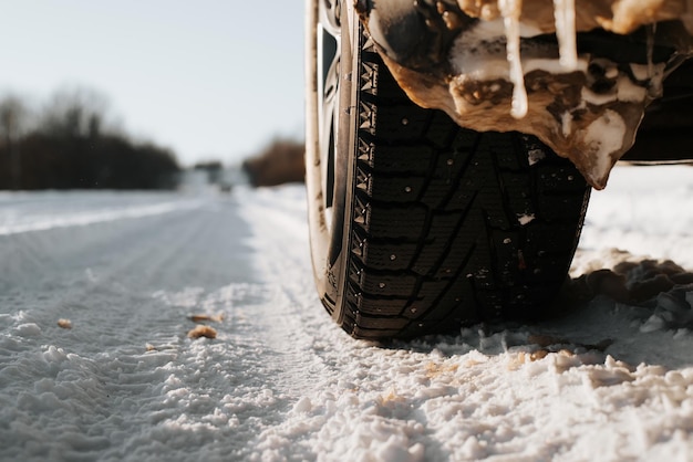 Pneumatici invernali chiodati della ruota dell'auto in piedi su strada innevata durante il giorno, spazio di copia. Primo piano, inquadratura dal basso.