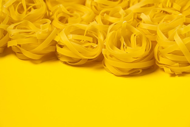 Pochi nidi di fettuccine fatti in casa isolati su sfondo giallo