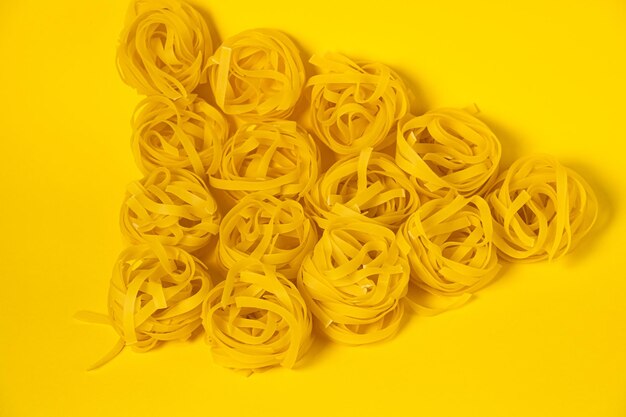 Pochi nidi di fettuccine fatti in casa isolati su sfondo giallo