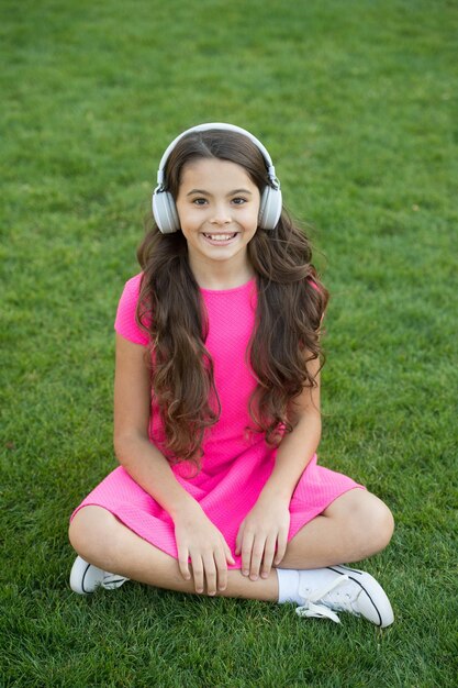 Podcast educativo La ragazza del bambino si diverte con la musica prato dell'erba verde Tempo piacevole La mia playlist estiva Ascolta la musica mentre ti rilassi all'aperto Le cuffie per bambini ascoltano la musica Le cuffie per ragazza ascoltano la musica