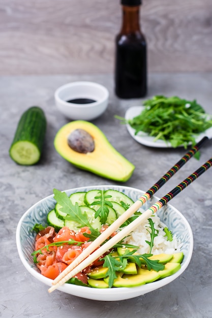 Poke di salmone con avocado, rucola e cetriolo in una ciotola e bacchette