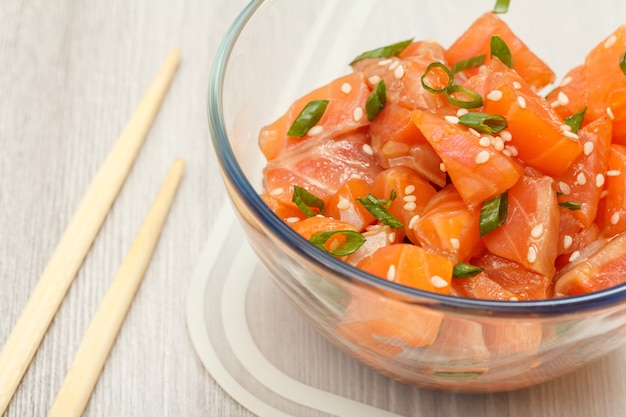 Poke di salmone hawaiano con cipolle verdi e semi di sesamo in una ciotola di vetro con bacchette. Vista dall'alto. Frutti di mare biologici