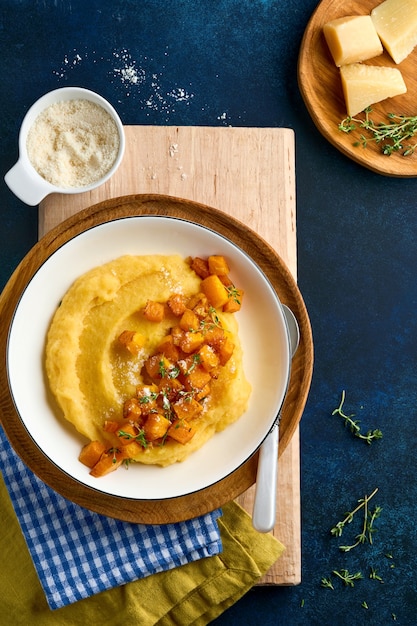 polenta con burro, zucca, aglio, santoreggia e parmigiano in ciotola bianca su blu