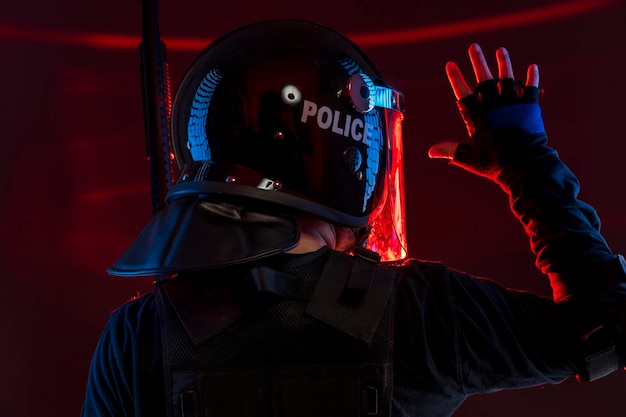 polizia che segnala ai loro compagni, poliziotto con equipaggiamento completo per anti-sommossa, forze dell'ordine in uniforme protettiva pronto per il controllo della folla isolato su nero