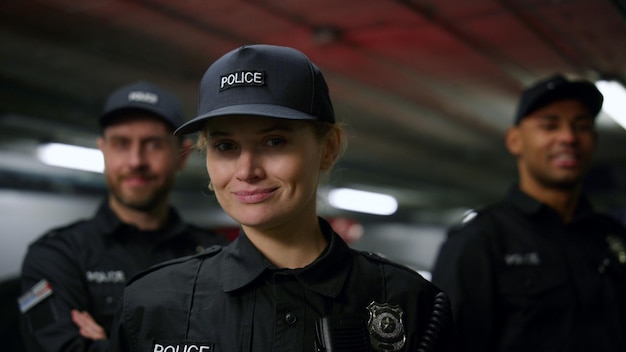 Poliziotta sorridente che guarda la telecamera Ritratto di un agente di polizia in servizio che posa con i colleghi sullo sfondo Poliziotta in uniforme di polizia con espressione facciale positiva
