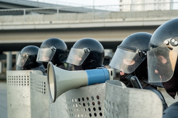 Poliziotto in casco antisommossa in piedi tra i colleghi con scudi antisommossa e parlando nel mefaphone mentre neutralizza i terroristi