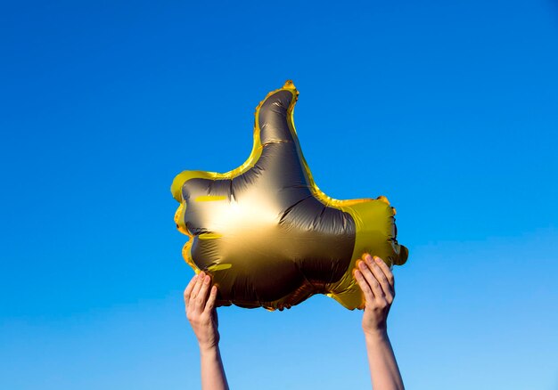 Pollice d'oro in su come palloncini tenuti contro un cielo estivo blu brillante