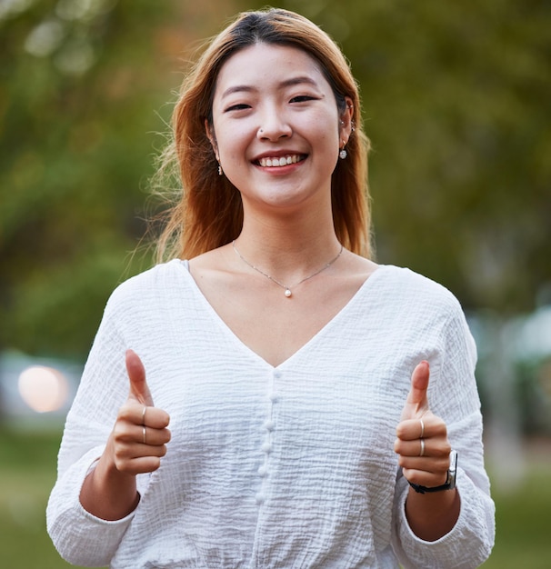 Pollice in alto felice e ritratto di donna asiatica nel parco per il supporto relax e felicità all'aperto Sorriso natura e volto di persona femminile con gesto della mano per accordo grazie e sì segno