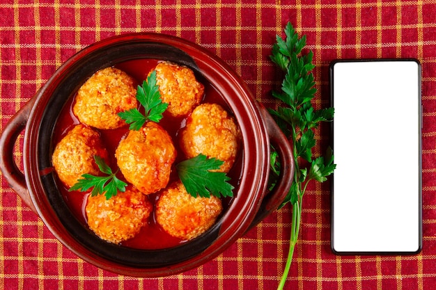 Pollo a polpette in salsa di pomodoro e smartphone con schermo bianco vuoto