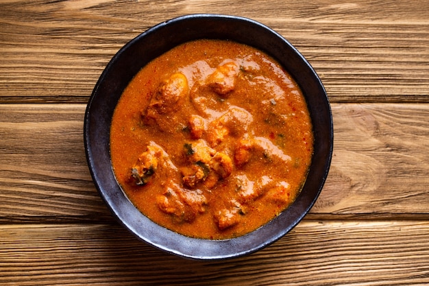 Pollo al curry indiano con sugo di pomodoro su fondo rustico in legno. Piatto tradizionale indiano pollo al burro tikka masala, pranzo o cena sani. Vista dall'alto