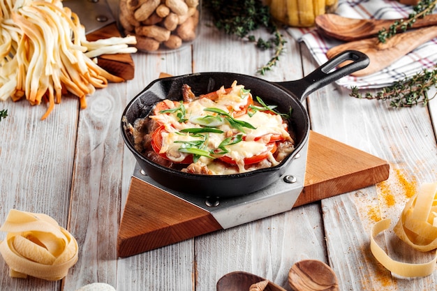 Pollo al forno con pomodori e formaggio in padella di ghisa sul tavolo in legno decorato