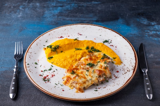 Pollo al forno sotto formaggio con purea di carote servito con forchetta e coltello